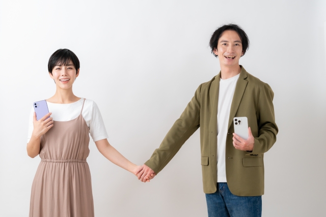 スマホを手に持ち手をつなぐカップルの画像