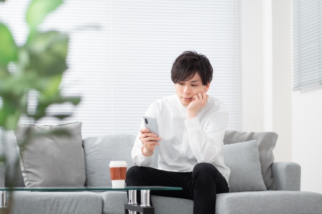 ソファに座ってスマホを操作する男性