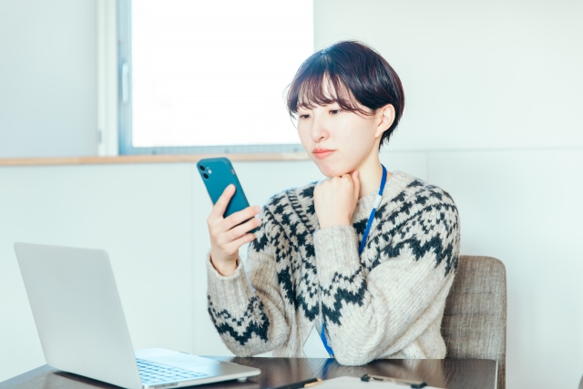 スマホを見ながらあごに手を当てて悩んでいる女性