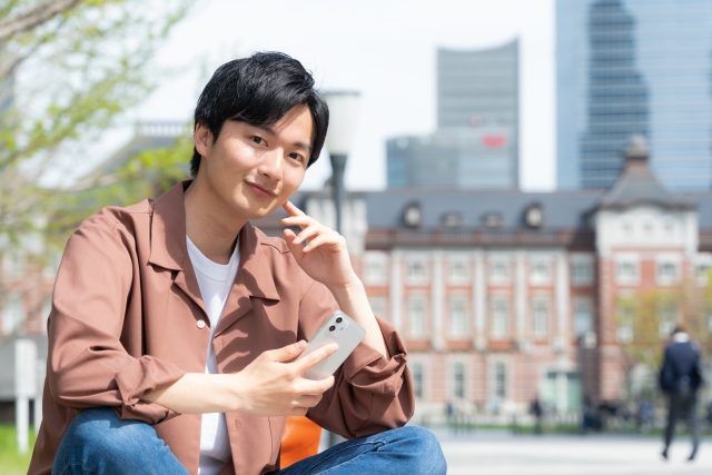 スマホを片手に持って座り、笑顔の男性
