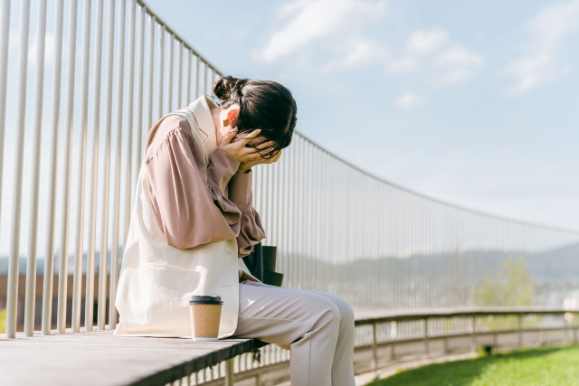 屋上で顔を手で覆い、悲しんでいる様子の女性