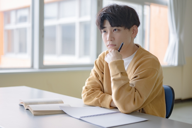 机の上にノートと教科書を出し、真剣に話を聞いている男性