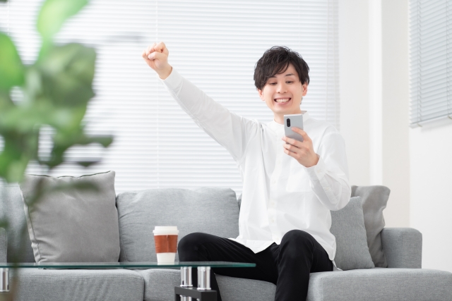 スマホを見ながらガッツポーズをする男性の画像