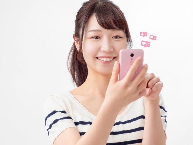 笑顔でスマホを操作する女性の画像
