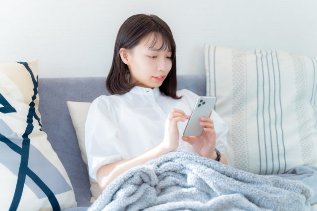 ソファでくつろぎながらスマホを操作する女性の画像
