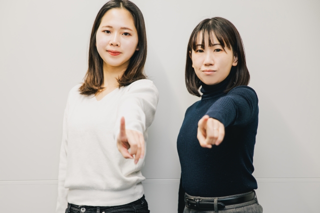 カメラに向かって指をさす仕草をする女性の画像