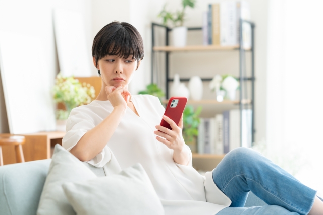 疑っている表情でスマホを見ている女性の画像