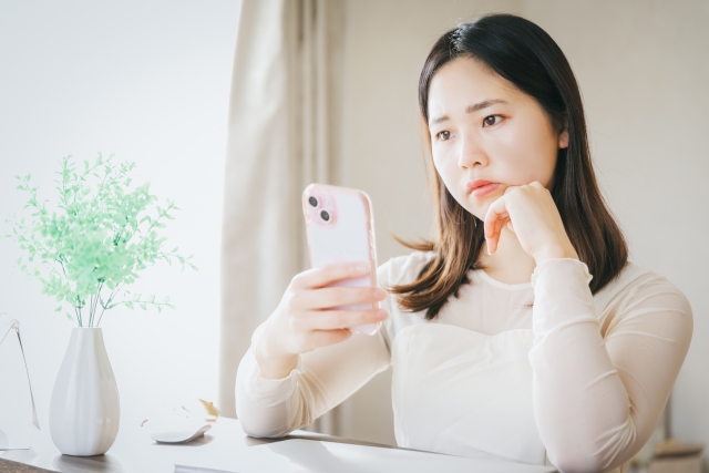 悩んだ表情でスマホを見ている女性の画像