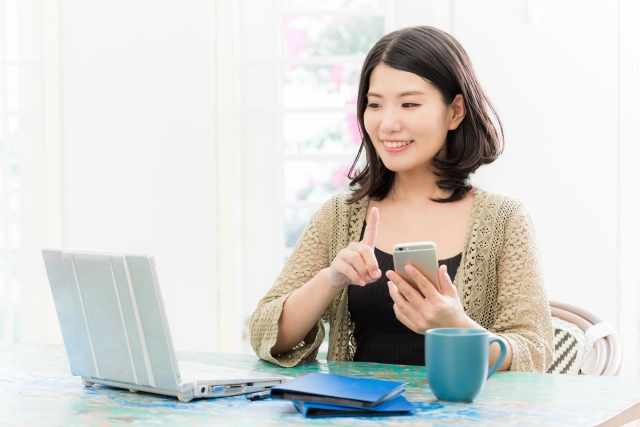 PCを見ながらスマホを操作する女性の画像