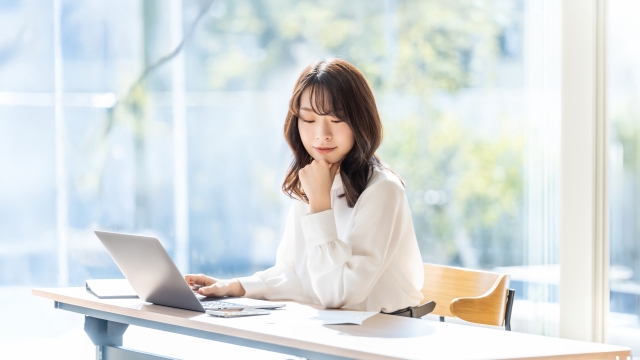 パソコンを見ながら考えている表情の女性の画像