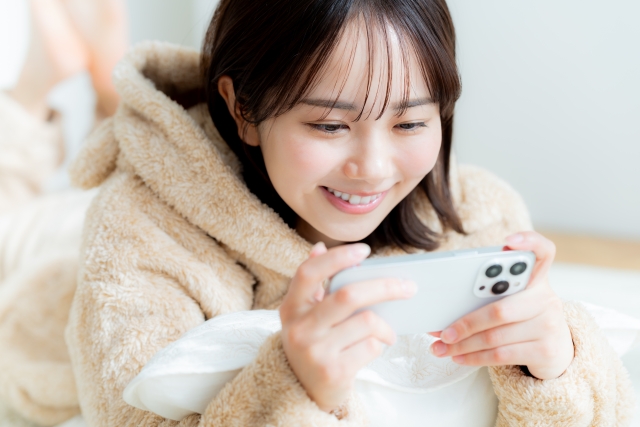 寝そべった姿勢でスマホを操作する女性の画像