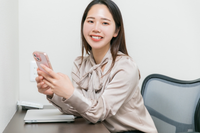スマホを手に持ち笑顔の女性の画像