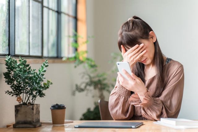 スマホを手に頭を抱えている女性の画像