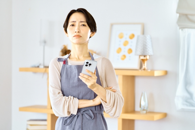 スマホを手に持ち難しい表情をしている女性の画像