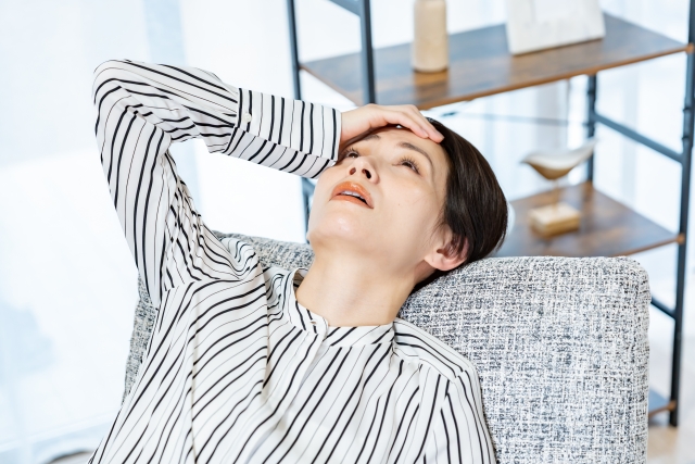 ソファに持たれて頭を抱える女性の画像