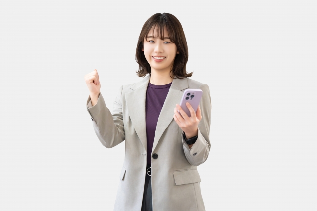 スマホを持ちガッツポーズをする女性の画像