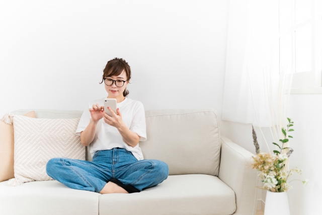 ソファに座ってスマホを操作する女性