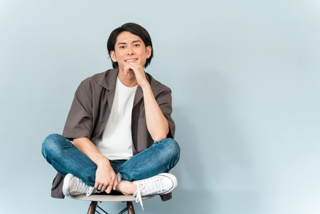 椅子の上であぐらをかいている笑顔の男性