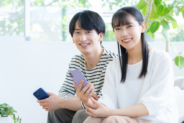 スマホを手に持ちカメラに向かって笑う男女