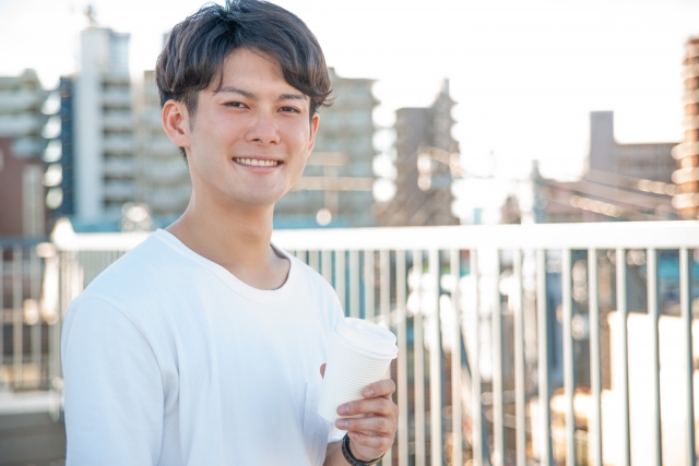屋外でテイクアウトの飲み物を手に持った笑顔の男性