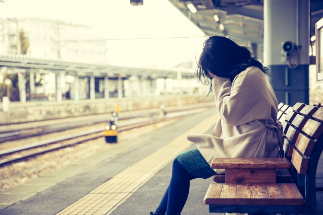 駅のホームのベンチに座って泣いている女性