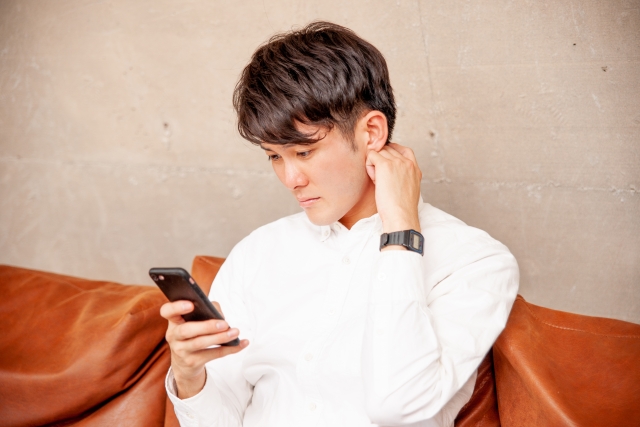 ソファに座ってスマホを困った表情で見ている男性