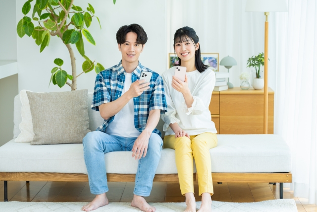 ソファに座ってスマホを持っているカップル