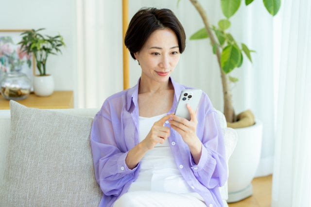 ソファに座ってスマホを見ている女性