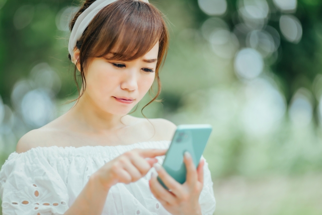 スマホを見て悩んでいる表情の女性のイメージ画像