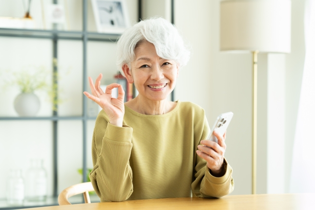 スマホを手に持ちオッケーサインをする中高年女性