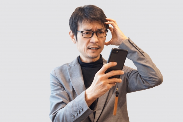 スマホを見て困った表情をしている中高年男性