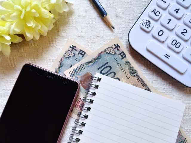 1,000円札の上に乗ったスマホとメモ帳の画像