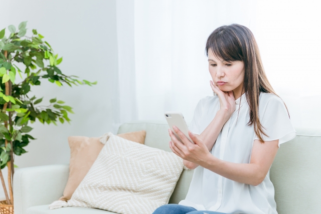 ソファに座って、スマホを悩んだ表情で見ている女性