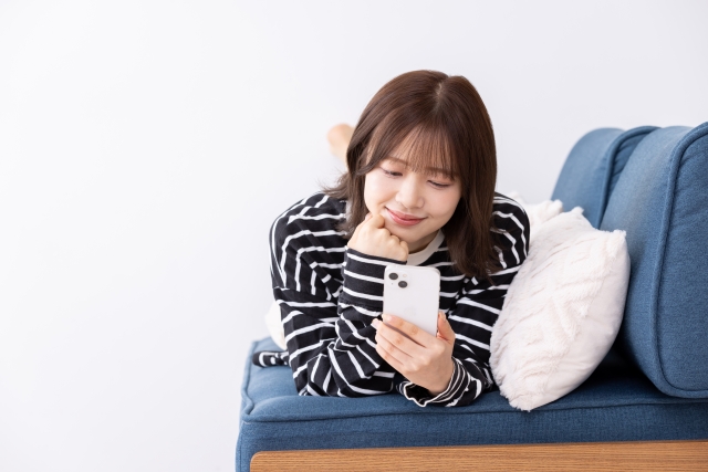 ソファに寝そべってスマホを見ている女性