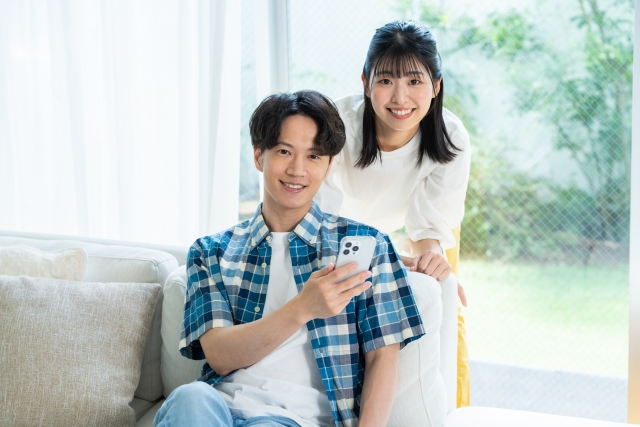 スマホを手に持ち、笑顔でカメラ目線の若いカップル