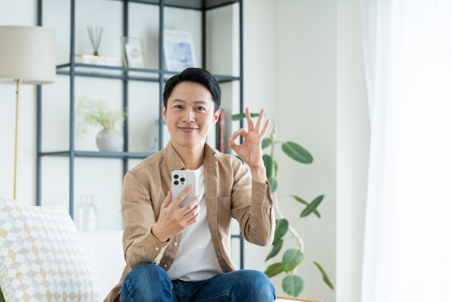 スマホを手に持ち、オッケーサインをする男性