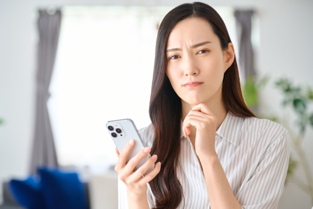 スマホを手に持ち悩んだ表情の女性の画像