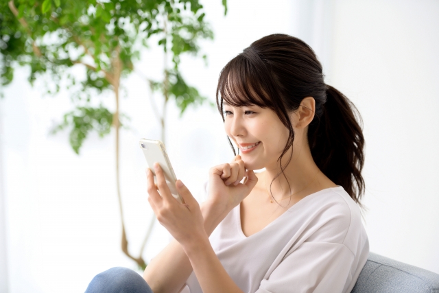 笑顔でスマホを操作する女性の画像